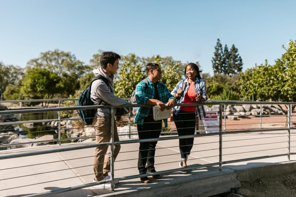Three college students enjoying a conversation on a sunny day on campus bridge.
